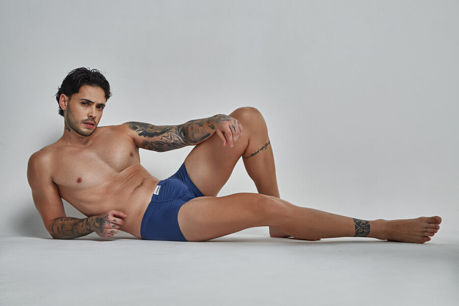 Gel o cera para el cabello masculino - Hombre en ropa interior azul recostado sobre fondo gris claro