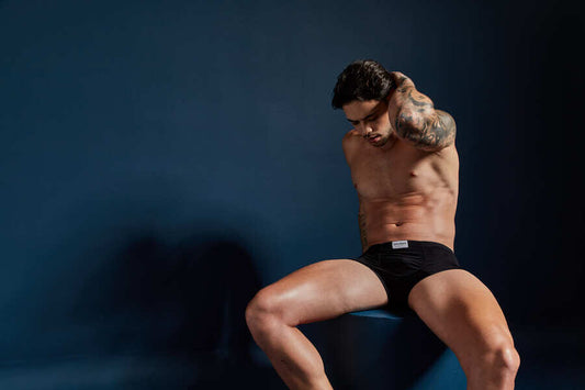 Beneficios de ser soltero - Hombre en ropa interior negra sentado frente a fondo azul oscuro