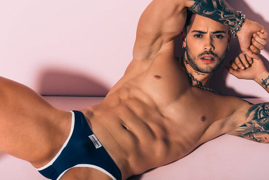 Cómo doblar ropa interior de hombre - Hombre en ropa interior azul marino, posando sobre fondo rosa.
