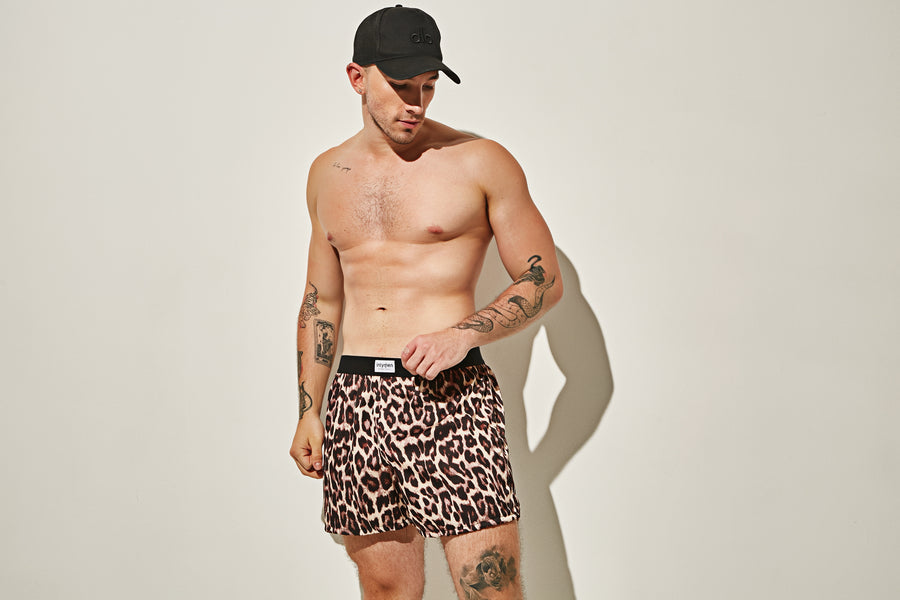 Hombre sin camisa con bóxer corto de estampado animal y gorra negra.