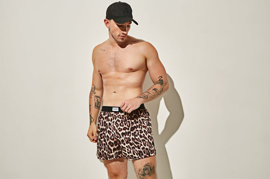 Hombre sin camisa con bóxer corto de estampado animal y gorra negra.