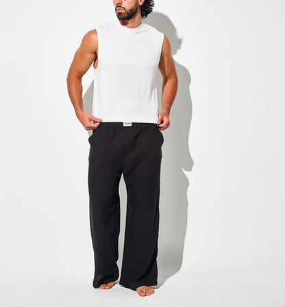 Hombre usando camisilla blanca sin mangas y pantalón negro tipo pijama, conjunto cómodo para descansar